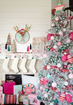 a christmas tree decorated with pink, green and white ornaments in front of a fireplace