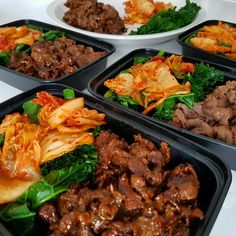 four black trays filled with different types of food on top of a white table