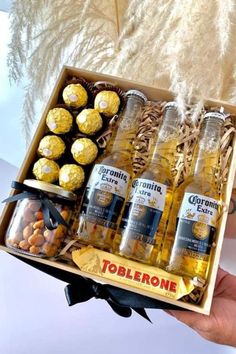 a person holding a wooden box filled with bottles and snacks in front of some feathers