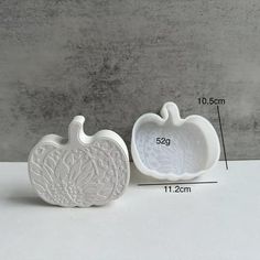 two white pumpkin shaped dishes sitting next to each other on top of a gray table