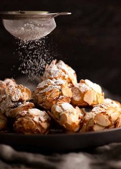 powdered sugar being sprinkled onto pastries on a plate