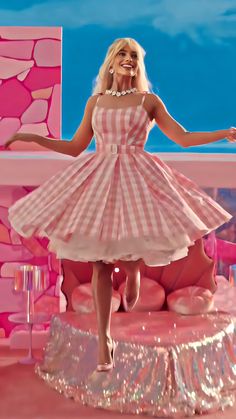 a woman in a pink and white dress is standing on a stage with her arms outstretched