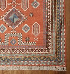 an orange and blue rug with fringes on the floor in front of a wooden wall