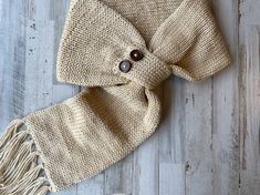 a knitted scarf with buttons and fringes on a wooden floor, top view