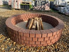 a brick fire pit sitting on top of gravel next to rocks and wood logs in the middle