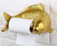 a gold fish toilet paper holder on a white tile wall with a roll of toilet paper in it's mouth