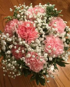 a bouquet of pink carnations and baby's breath on a wooden table