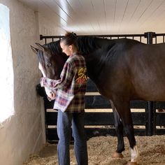 a woman standing next to a brown horse in a stable with hay on the floor