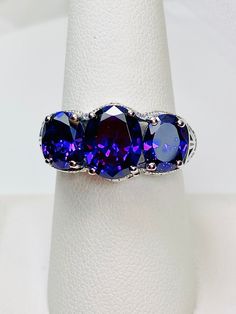 Purple CZ Ring 3Stone Design#36 Custom Made Inspired by Edwardian/Art Deco era, I now offer this exquisite reproduction ring in sterling silver. The full oval cut gemstone in the center is 10mm x 8mm and is approximately 2.5 carats, the 2 gemstones on each side are 8mm x 6mm, and are approximately 1 carat each. The gemstones together are approximately 4.5ctw to 5ctw. The 3 stones together, east west on the finger, are 20mm (13/16th of an inch) across. These Purple stunning gemstones have excelle Oval Tanzanite Sapphire Ring, Oval Sapphire Ring With Intricate Design, Exquisite Oval Filigree Promise Ring, Exquisite Silver Oval Sapphire Ring, Exquisite Oval Tanzanite Rings, Exquisite Oval Amethyst Ring For Anniversary, Exquisite Oval Sapphire Ring In Silver, Heirloom Style Oval Amethyst Sterling Silver Ring, Heirloom Style Oval Amethyst Ring In Sterling Silver