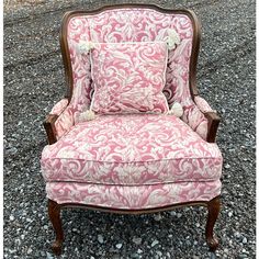 a pink and white chair with a pillow on it's back sitting in gravel