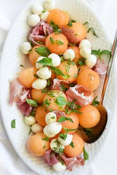 a white plate topped with oranges and other food on top of a table next to a spoon