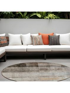 a large white couch with many pillows on it's back and sides, sitting in front of a plant wall