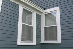 two windows on the side of a gray house with white trim and shutters that are open