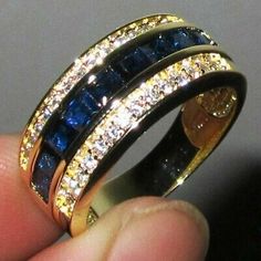 a gold ring with blue and white stones on it's sides, in someones hand