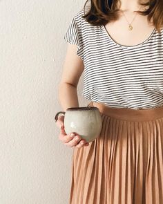 a woman is holding a cup in her right hand and wearing a striped t - shirt