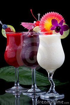 three different colored cocktails are lined up on a black surface with leaves and flowers