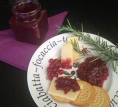 a white plate topped with crackers and fruit next to a jar of jam on a purple napkin