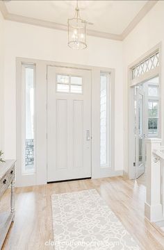 a white entryway with an ornate rug and chandelier