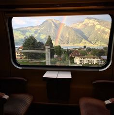 a rainbow seen through the window of a train with mountains and houses in the background