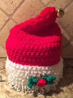 a red and white knitted santa hat sitting on top of a tile counter next to a wall