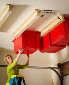 a woman standing on a step ladder holding two red bins above her head, with the bottom planks removed