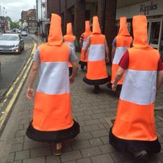 several people in orange vests walking down the street with traffic cones on their heads