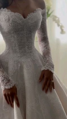 a woman in a white wedding dress with long sleeves and lace on her arms is posing for the camera