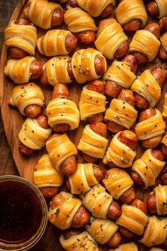 hotdogs wrapped in bread on a wooden platter next to a cup of sauce