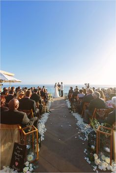 a wedding ceremony on the beach with people sitting in chairs and looking at the water