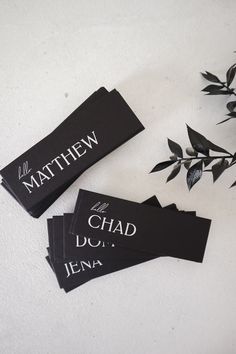 three black tags with the names of different brands on them next to some flowers and leaves