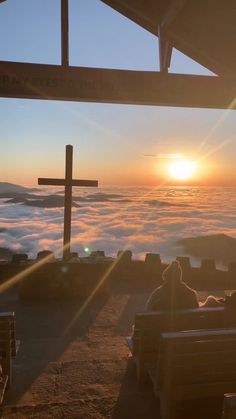 people sitting on benches at the top of a hill with a cross in the background