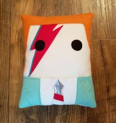 a pillow made to look like an animal with a red nose and blue tail, sitting on a wooden floor