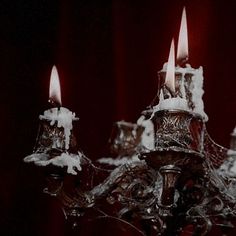 a chandelier with four lit candles in the middle and red curtains behind it