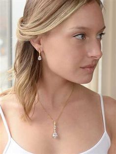 a woman with blonde hair wearing a white tank top and gold earrings, looking off to the side