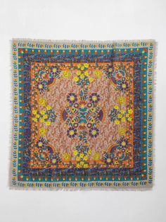 an orange, yellow and blue rug with fringes on the edges is hanging up against a white wall