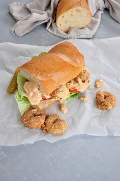 a sandwich with chicken and lettuce sitting on wax paper next to some bread crumbs