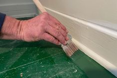 a man is painting the wall with a paintbrush and green flooring padding