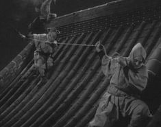 an old black and white photo of two men on a roof with one holding onto the rope