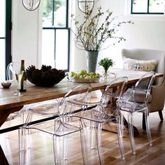 a dining room table with clear chairs and fruit on the table in front of it