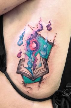 an open book tattoo on the side of a woman's stomach with watercolor splashes