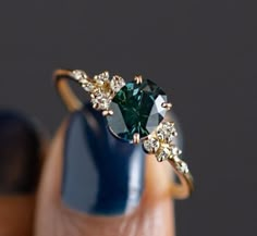 a woman's hand holding a ring with a green stone and white diamonds on it