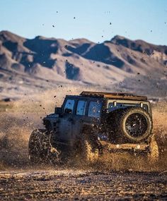 a jeep driving through the desert with mountains in the background