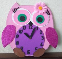 a pink clock with an owl face and flower on it's face, sitting on a shelf