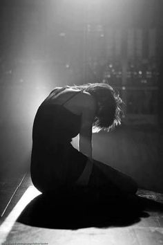 a woman sitting on the floor in front of a light that is shining down over her head