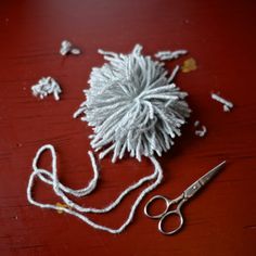 a pair of scissors sitting on top of a wooden table next to yarn and needles