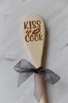 a wooden spoon with the words kiss my cook written on it and a bow tie