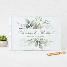 a wedding guest book next to a pen and succulent