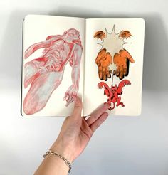 a hand is holding an open book with drawings on it and the pages are red