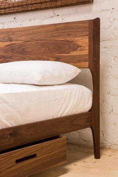 a bed with white pillows and wooden headboard next to a brick wall in a bedroom