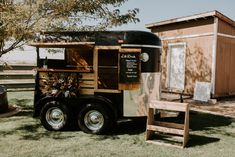 a food truck parked in the grass next to a wooden chair and tree stumps